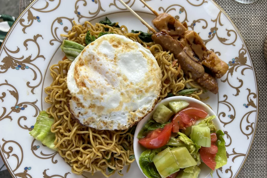 A plate of traditional Indonesian food, including mie goreng and satay skewers.