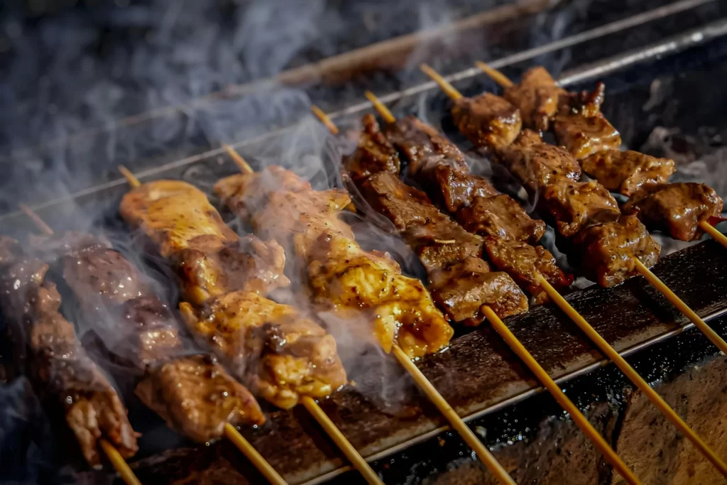 Satay skewers smoke on a grill