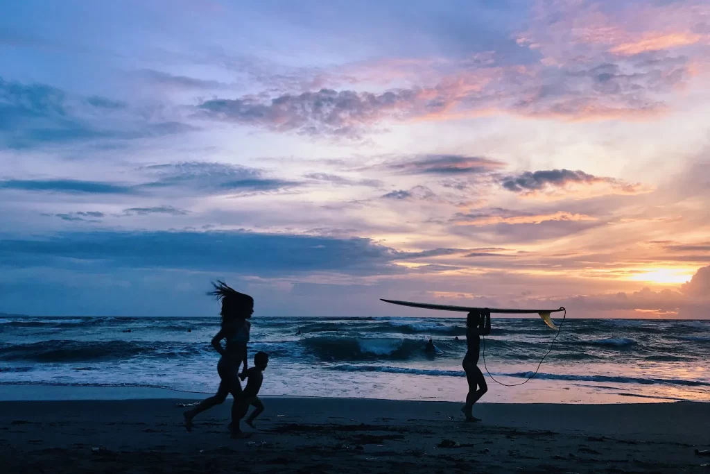 Silhouettes of children and surfers against a sunset on Batu Bolong beach in Bali, Indonesia.