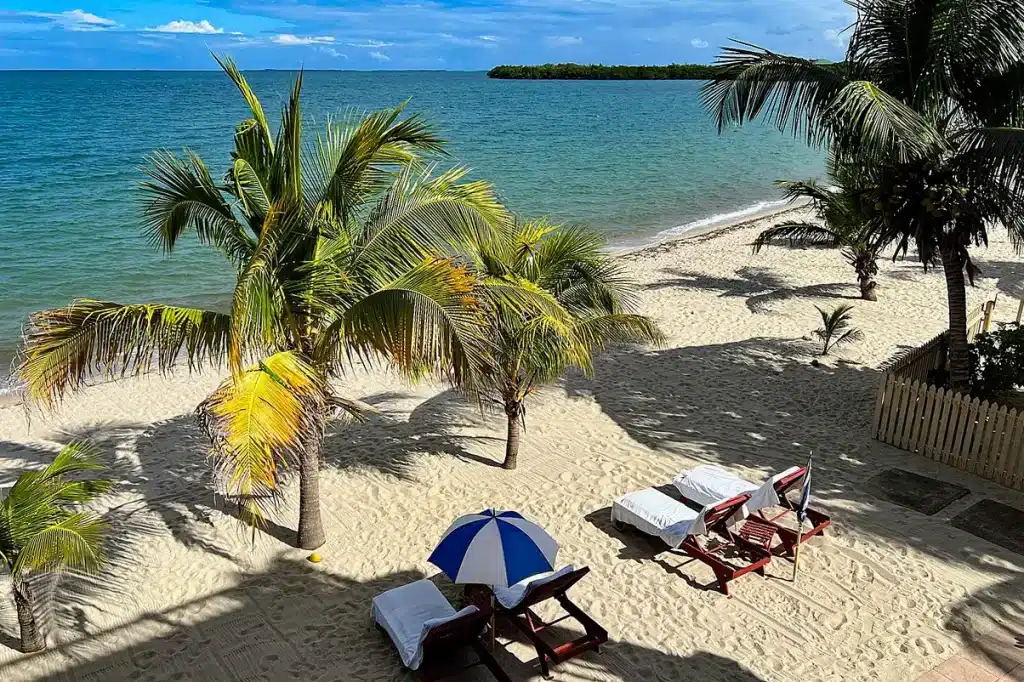 Lounge chairs and an umbrella line a white sand beach near Placencia, Belize.