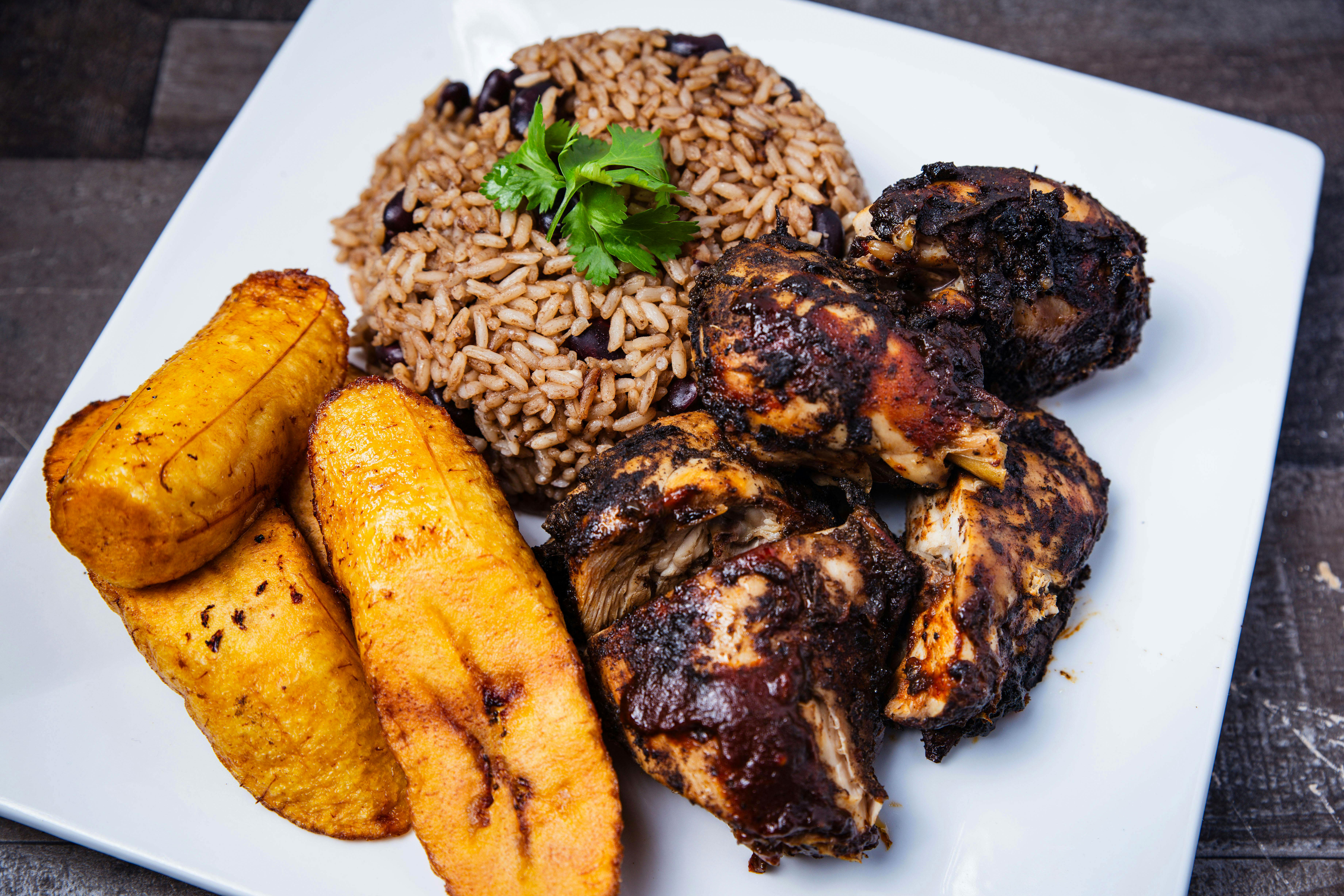 Traditional Belizean cuisine of rice and beans, stewed chicken, and fried plantains on a plate.