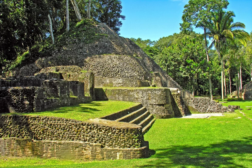 Ancient stone temples and walls stand against a jungle background in Caracol, Belize. When comparing Tikal vs. Caracol and which to visit, Caracol's less-touristed path is advantageous to some.