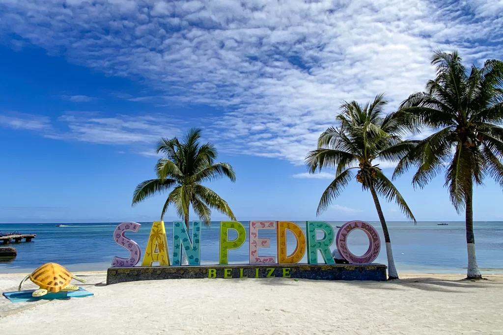 A cheerful sign spelling out "San Pedro" sits on the beach underneath palm trees in San Pedro, Belize.