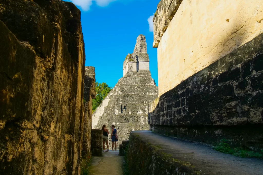 Two tourists stand in the shadow between two ancient Mayan pyramids in Tikal, Guatemala.