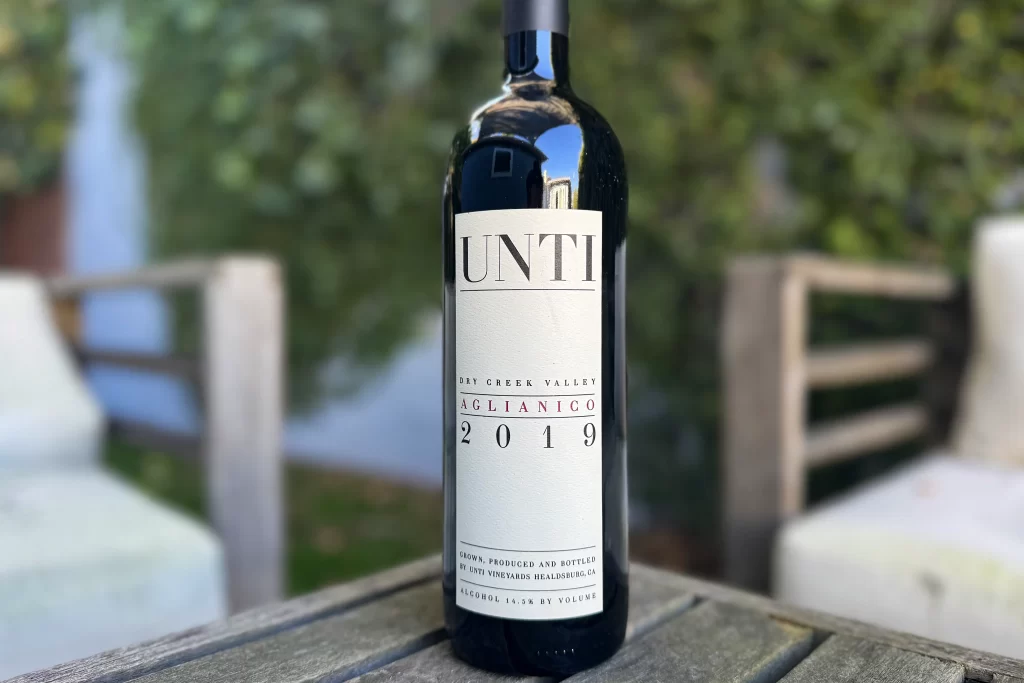 A bottle of red wine from Unti Vineyards sits on a wooden patio table.