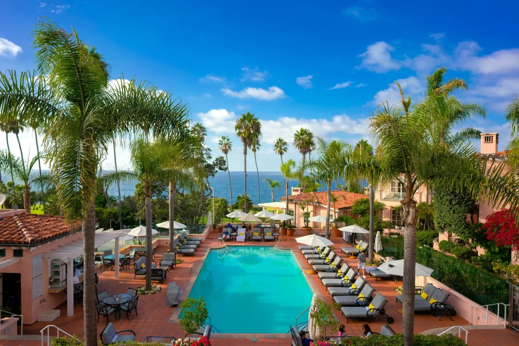 Palm trees line the pool at the Valencia Hotel in La Jolla, California, with views of the Pacific Ocean beyond.