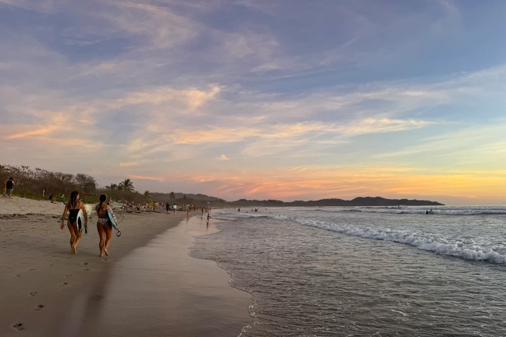 Two girls carry surfboards along the shoreline of Guiones, Costa Rica at sunset. The Guiones surfing break is one of the most popular near Nosara.