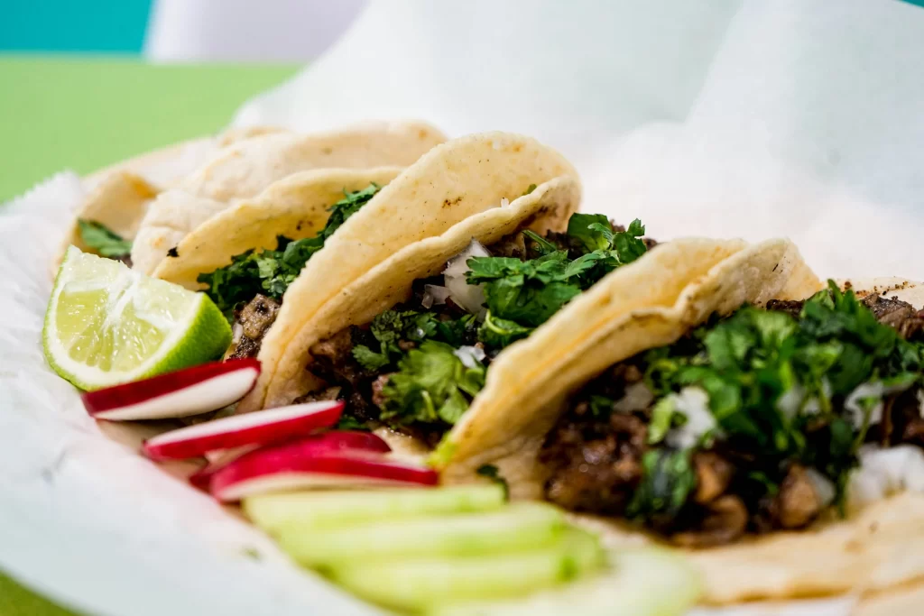 A plate of street tacos is accented by lime wedge and garnish.