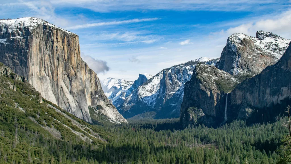 The iconic Tunnel View in Yosemite National Park shows the granite monolith of El Capitan on the left, and Bridalveil Falls cascading to the pine-covered valley on the right.