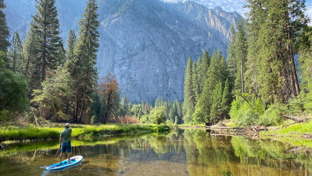 A lone paddle boarder paddles the serene waters of the Merced River in Yosemite Valley.