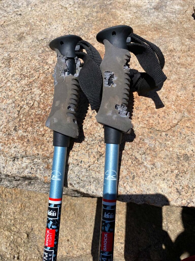 A hiker's trekking poles are shown up close, with the handles chewed by an animal.