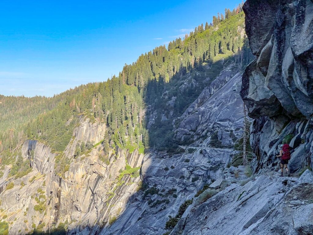 A hiker cuts along a narrow cliffside on the High Sierra Trail in Sequoia National Park.