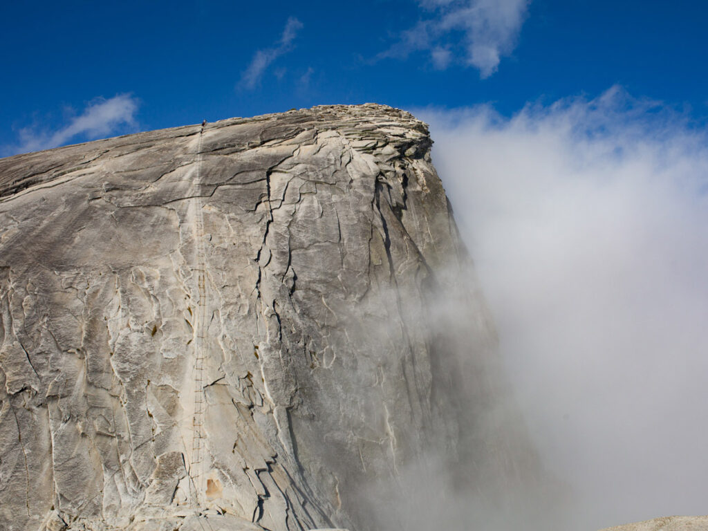 Hikers appear as minute specks, as they climb the vertical cables near the Half Dome summit. Half Dome is one of the most famous hard hikes in Yosemite National Park.