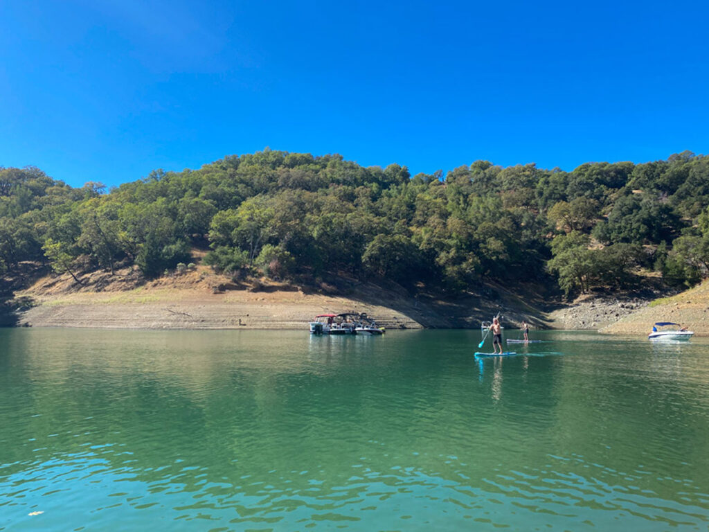 A paddle boarder is silhouetted against golden hills and oak trees on Lake Sonoma in Sonoma County, California.