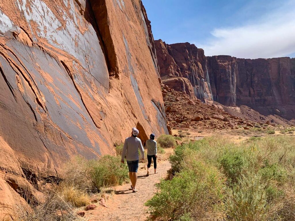 Two hikers walk along the dirt trail of Marble Canyon to view ancient Native American petroglyphs.