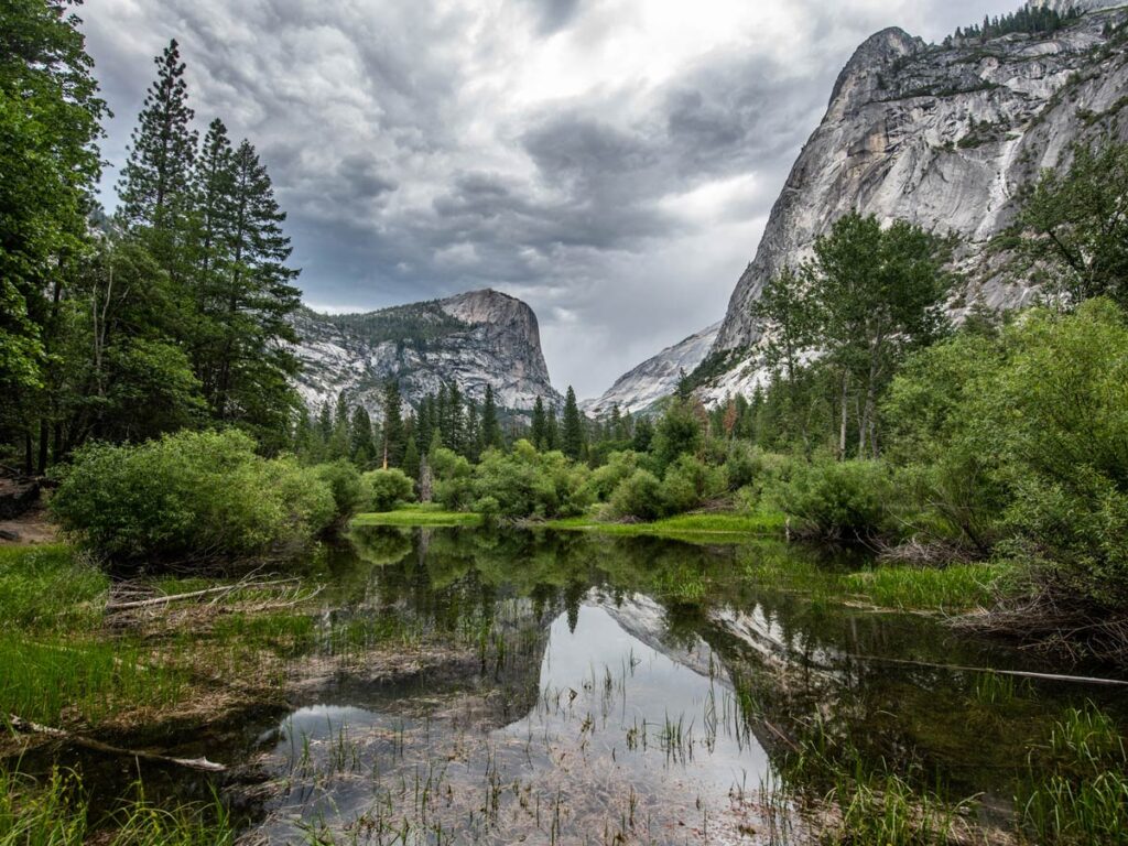 Mirror Lake on a cloudy day in Yosemite Valley, with the surrounding forests and mountains reflected on the water.