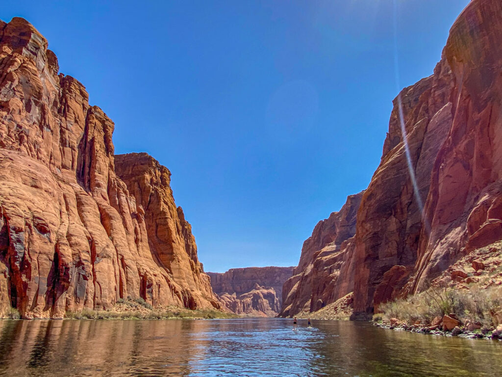 Two paddle boarders appear minute along the Colorado River, as it winds placidly through Marble Canyon's towering stone walls.