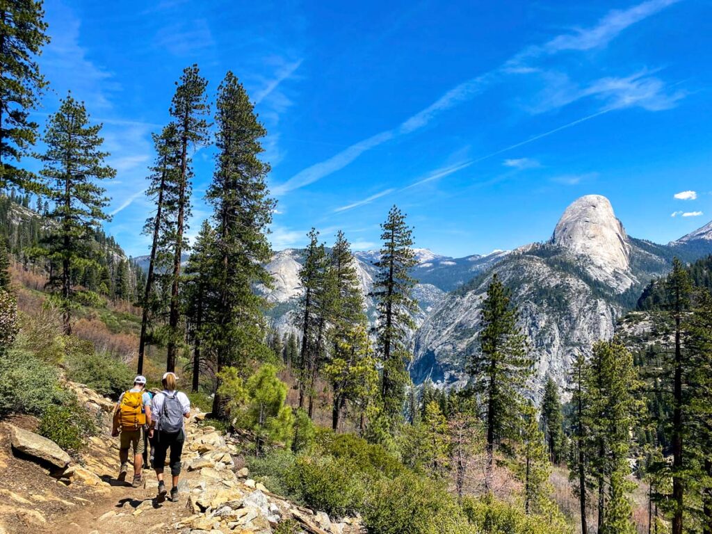 Hikers traverse the Glacier Point to Yosemite Valley trail with Half Dome prominent in the distance.