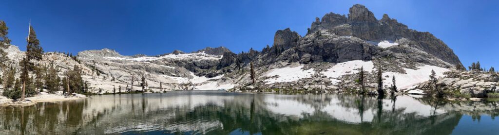 A panorama of Pear Lake in Sequoia National Park, with sparse pines and snowcapped peaks reflecting in the waters below.