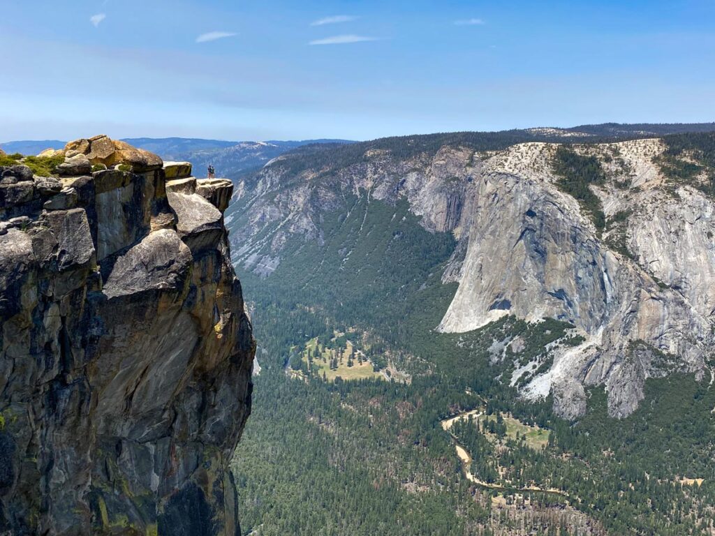 Two people stand at the edge of Taft Point, appearing miniscule against Yosemite Valley sprawling below. 