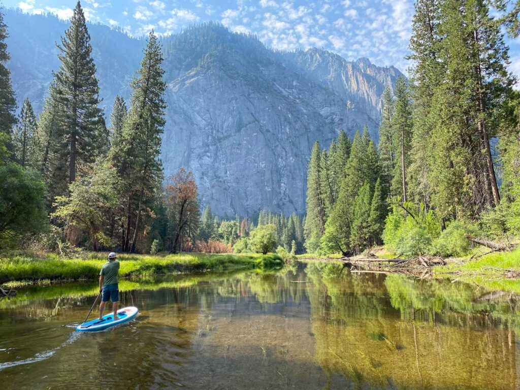 A lone paddle boarder paddles the serene waters of the Merced River in Yosemite Valley