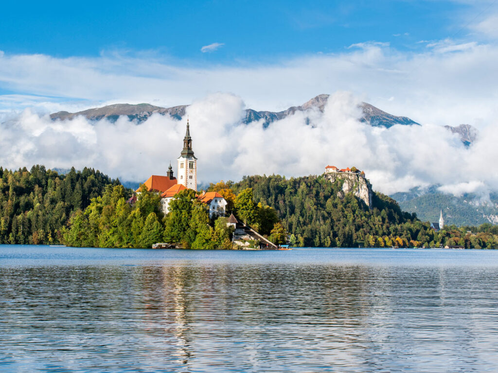 Church of the Assumption of Mary sits on Lake Bled, with Bled Castle behind.