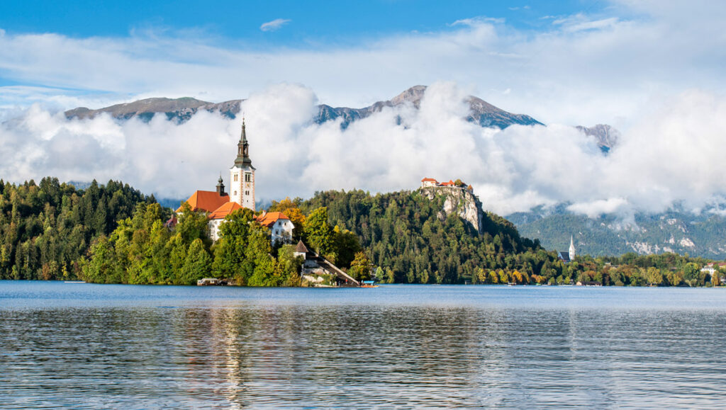 Church of the Assumption of Mary sits on Lake Bled, with Bled Castle behind.