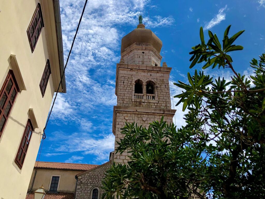 The old stone bell tower of Krk, Croatia as seen from street level.