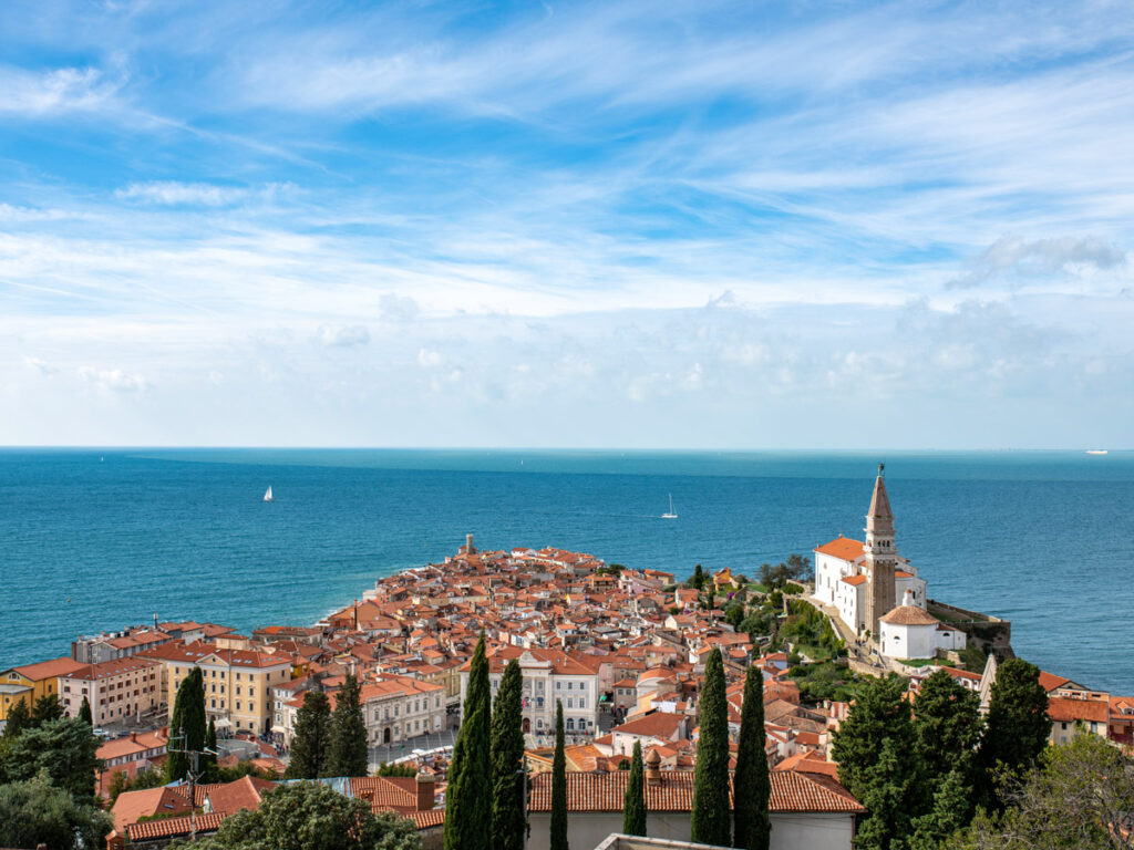 The terracotta rooftops of Piran, Slovenia as seen from the hills above town, silhouetted against the blue Adriatic Sea.