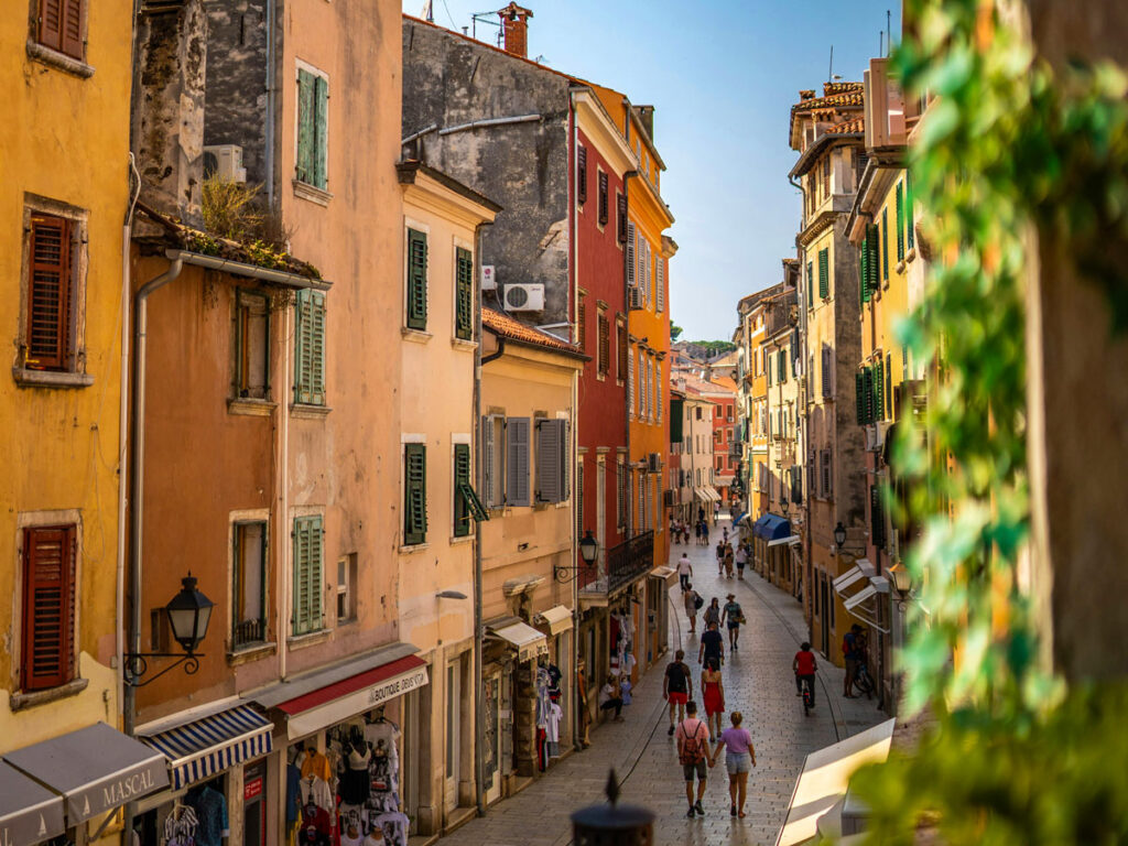 Tourists stroll beneath colorful facades in the old town of Rovinj, Croatia.