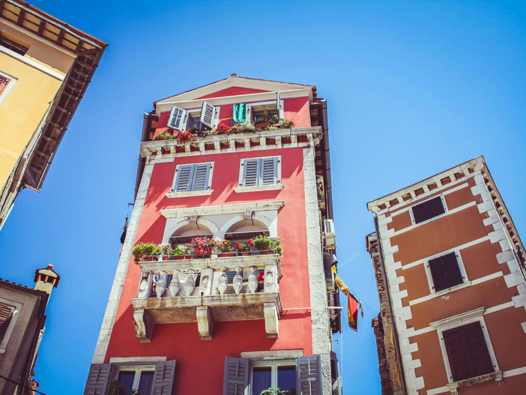 Tall colorful buildings with potted plants lining their balconies rise above the old town in Rovinj, Croatia.