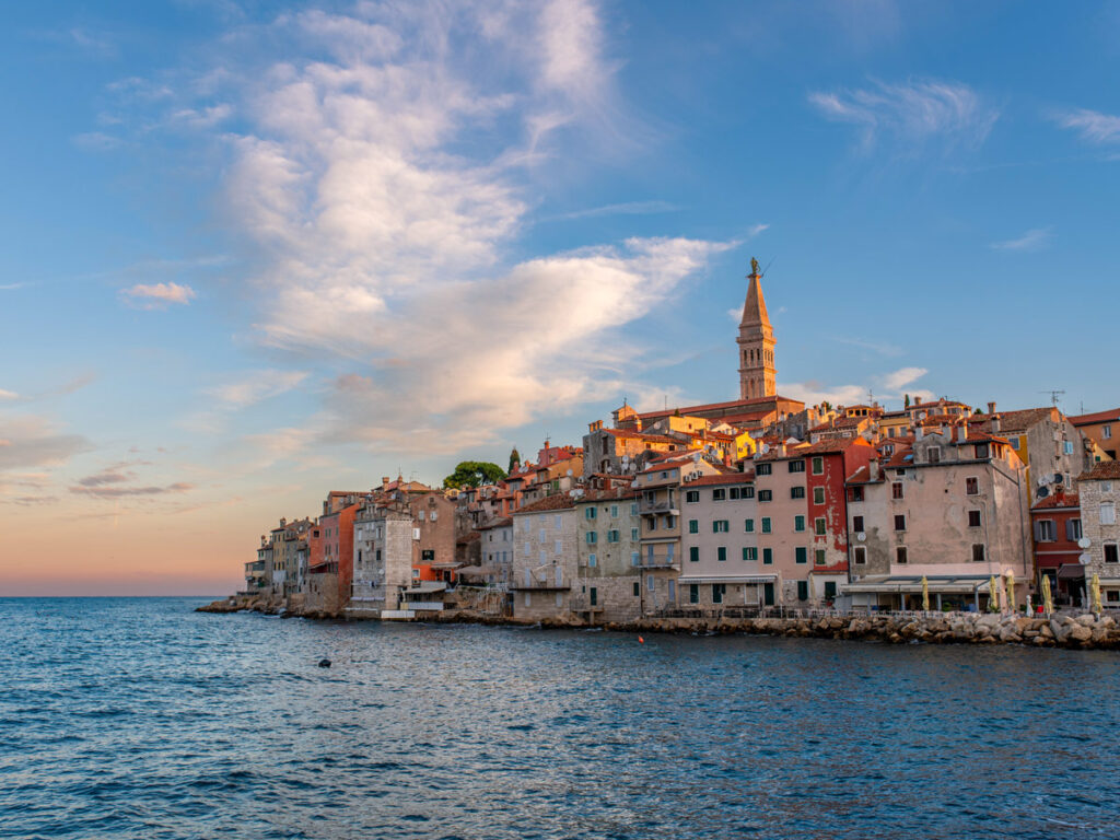 Pastel-colored buildings line the waterfront in Rovinj, Croatia at sunrise.