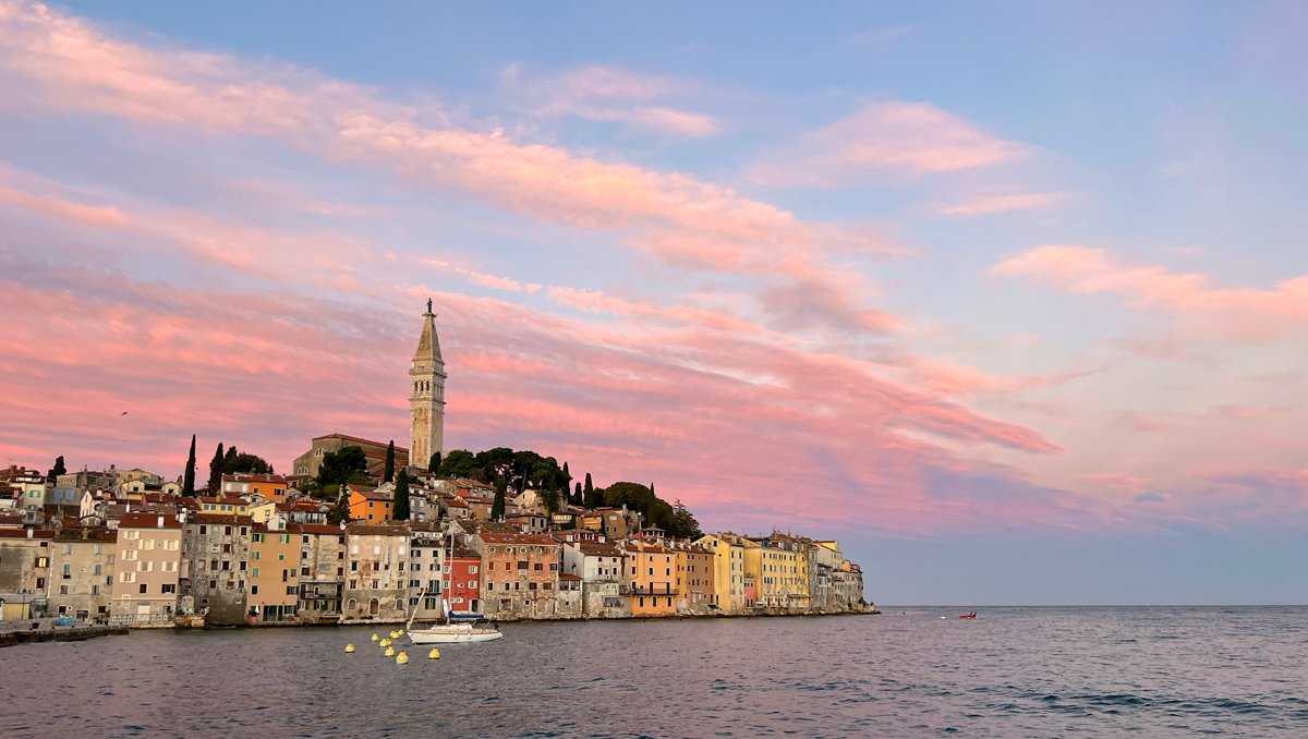 The old town of Rovinj, Croatia is silhouetted against a pink sky at sunrise