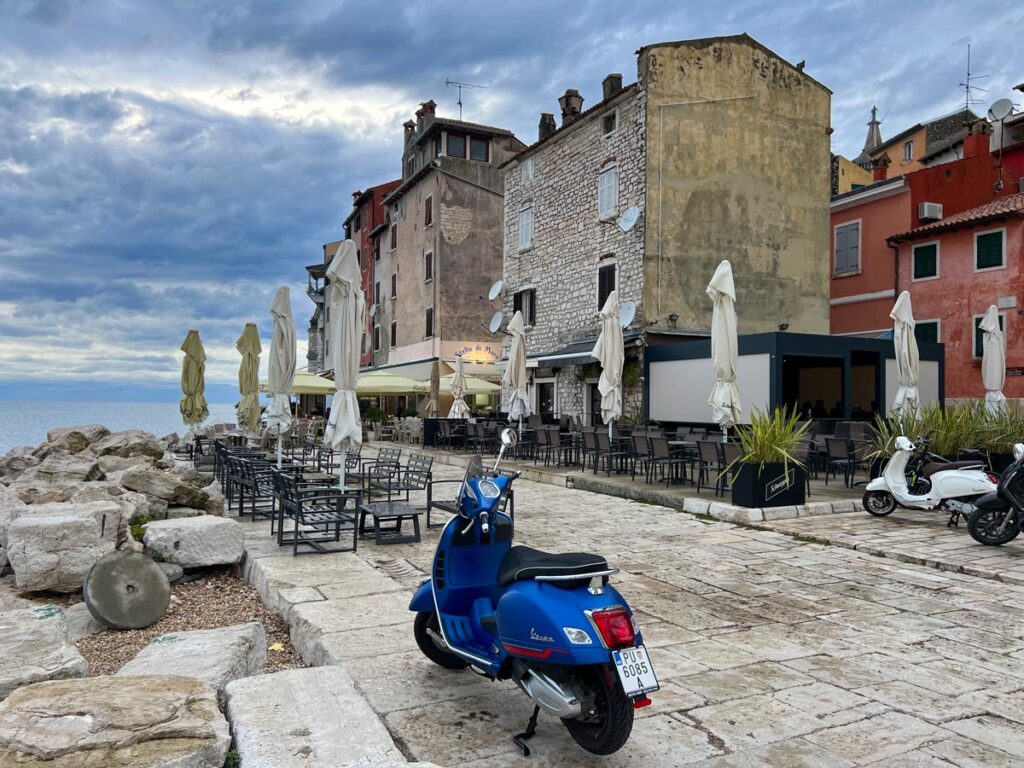 A blue Vespa rests along the old town's promenade in Rovinj, Croatia.