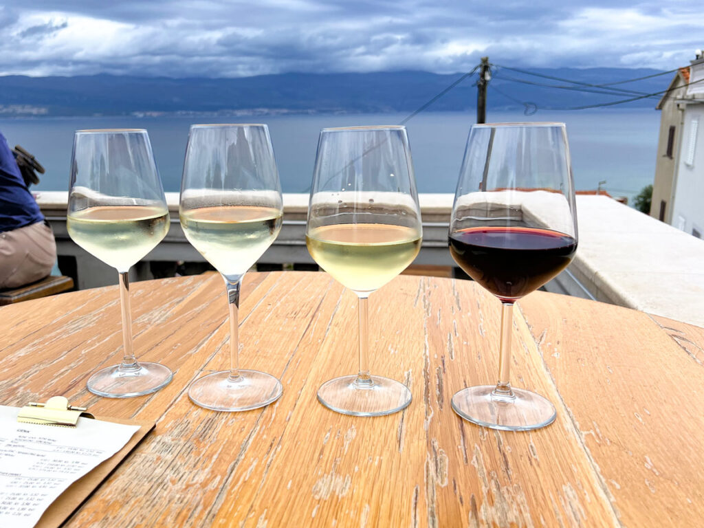 Four wine tasting glasses are lined on a table in Vrbnik, Croatia, with the Adriatic in the background.