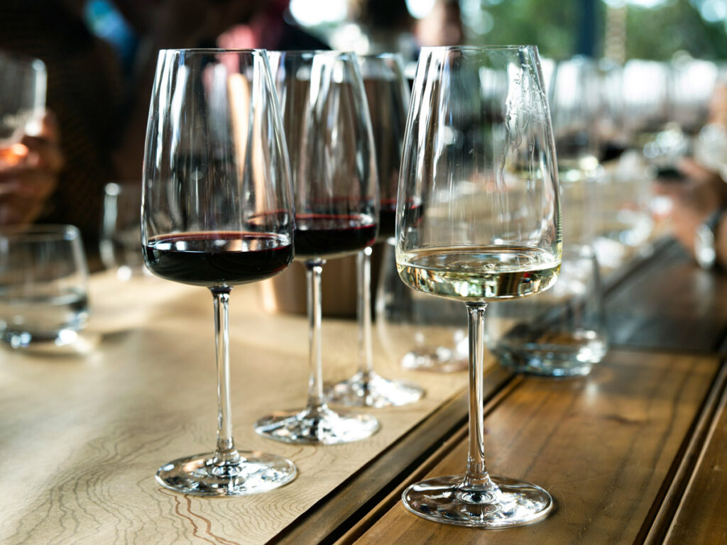 Three wine glasses, filled with red and white wines, rest on a table.