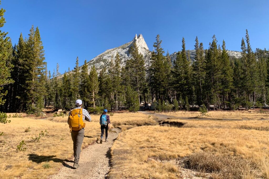 Two hikers traverse the Cathedral Lakes trail in Yosemite National Park, with Cathedral Peak in the background.