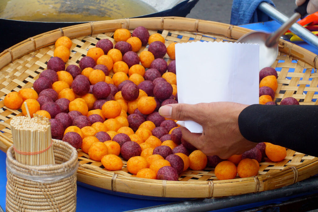 A vendor scoops up colorful fried sweet potato balls, a classic dessert of southeast Asia.