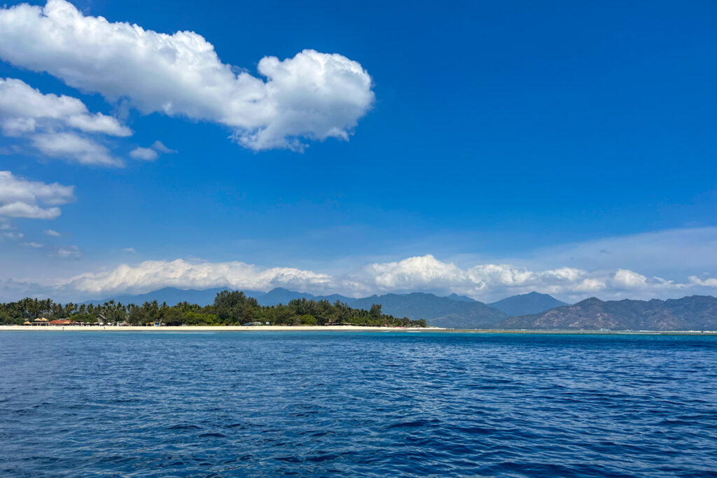 Indonesia's Gili Air island is seen from across the Lombok Strait against a bright blue sky.