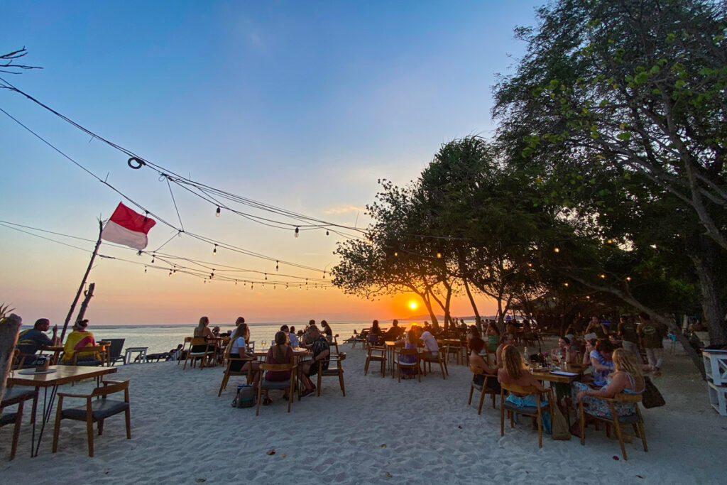 Tourists on Gili Air sit on the beach at sunset, dining at Mowie's bar and restaurant.