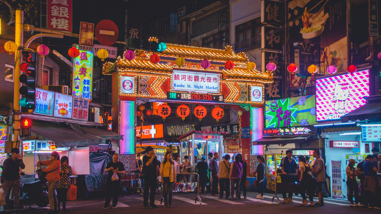 Pedestrians line the illuminated entry gate to Raohe Night Market in Taipei, Taiwan.