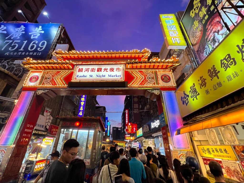 Pedestrians crowd under the illuminated entrance gate of Raohe Night Market in Taipei, Twaiwan.