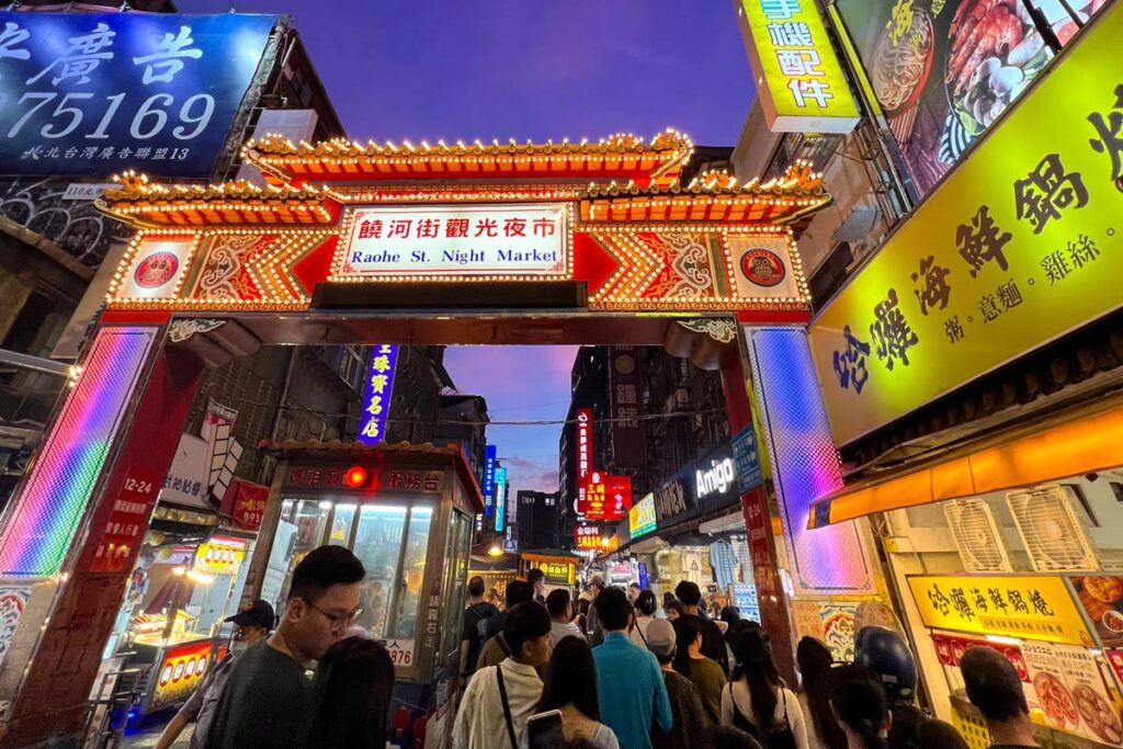 Pedestrians crowd under the illuminated entrance gate of Raohe Night Market in Taipei, Taiwan.