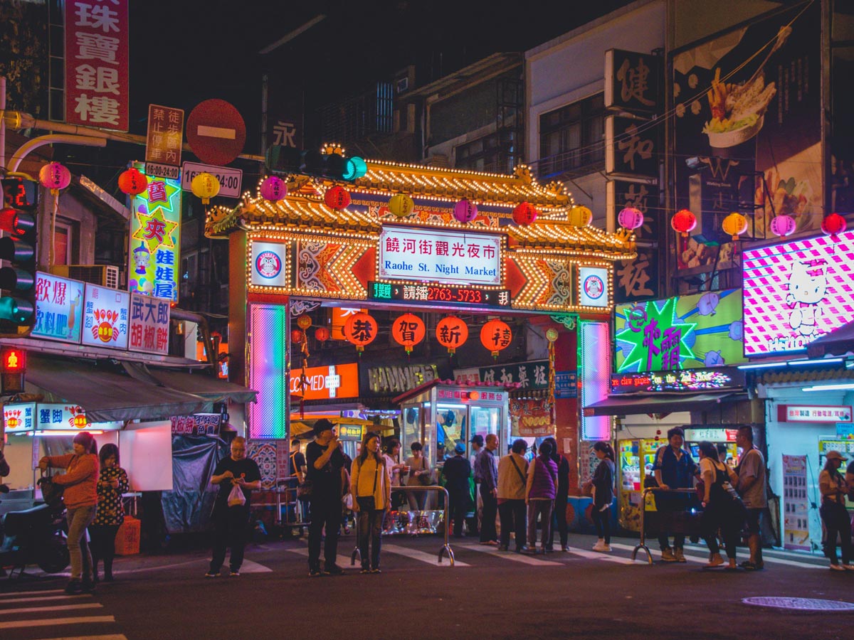 Pedestrians line the illuminated entry gate to Raohe Night Market in Taipei, Taiwan.