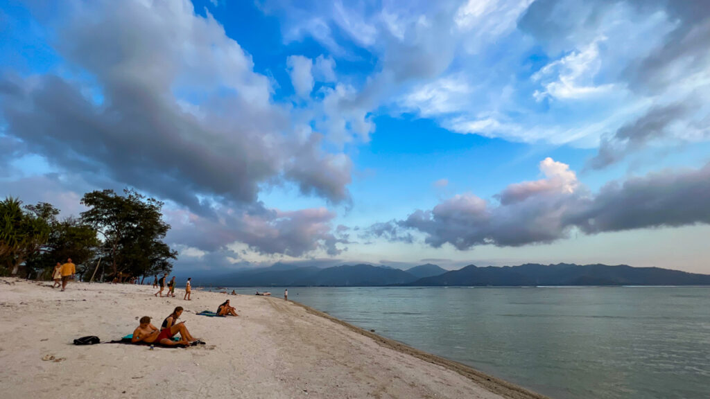 Tourists relax along the beach of Indonesia's Gili Air island, with the hills of Lombok visible across Lombok Channel.