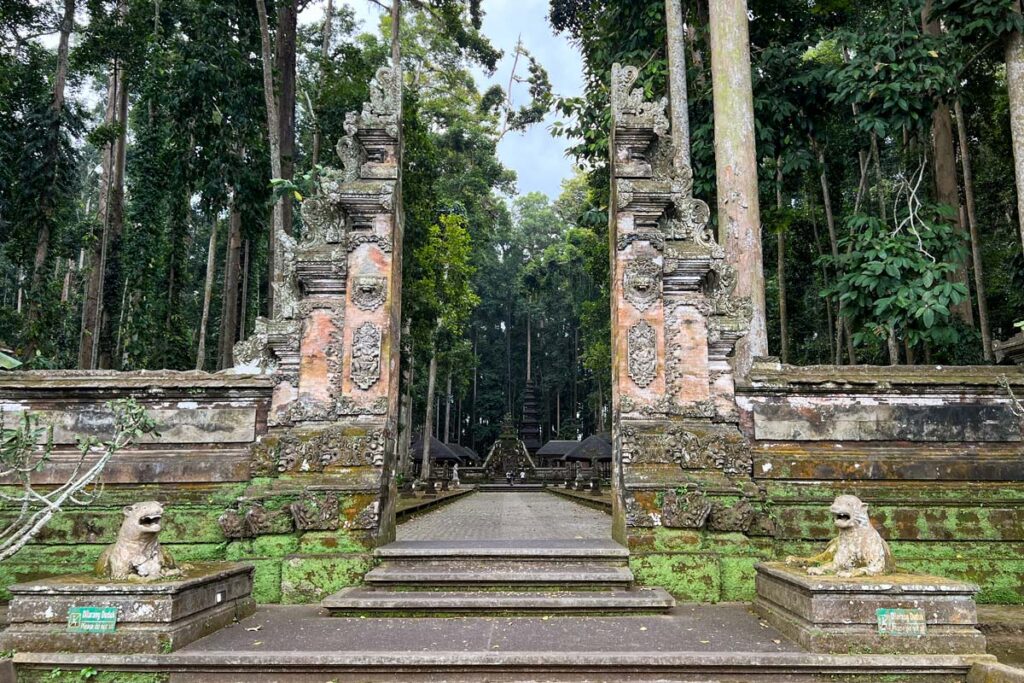 The entrance to Sangeh Monkey Forest outside of Ubud, Bali, is flanked by a brick and stone gate and stone monkey statues leading into the jungle.