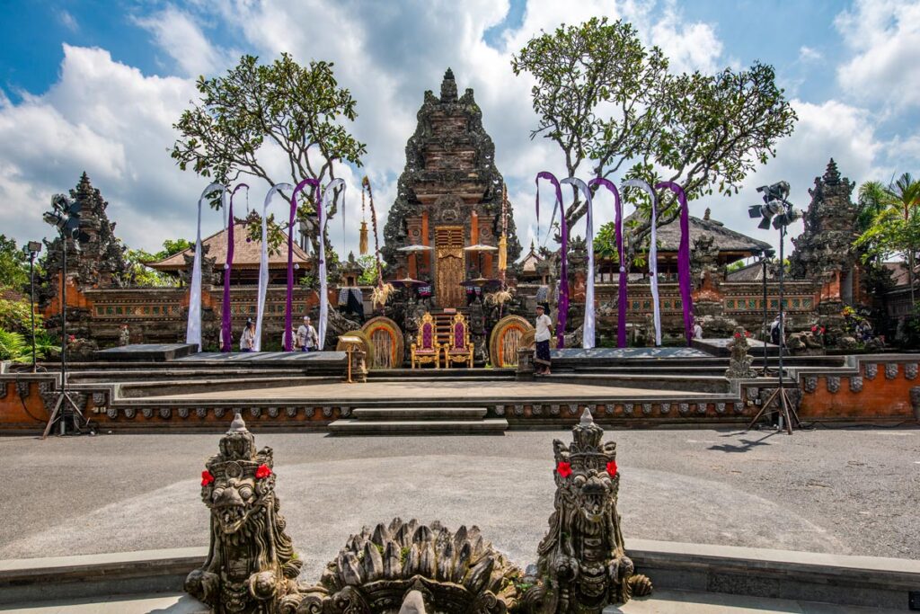 The entrance to Saraswati Temple in Ubud, Bali, is decorated with purple and white flags and two gold thrones at the base of the stone temple.