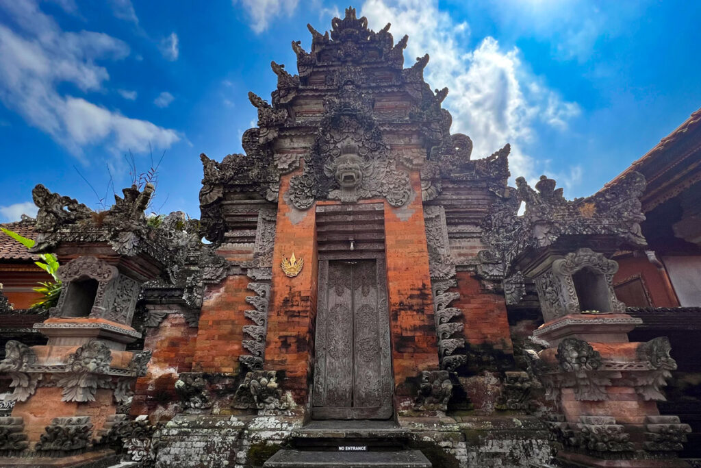 The intricate stone carvings of Ubud Palace in Bali, Indonesia, where a stone face adorns the top of a brick entryway.