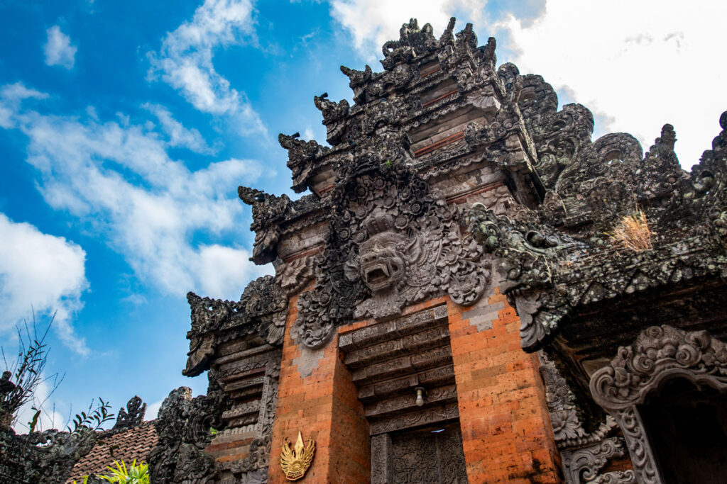 An angled close-up of the intricate brick and stonework of Ubud Palace in Bali, Indonesia, silhouetted against a bright blue sky.