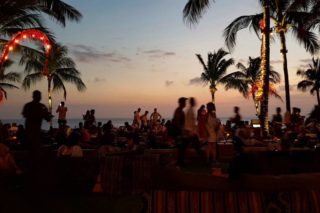 Revelers at a beach club in Seminyak, Bali, silhouetted against a dark sky at dusk.